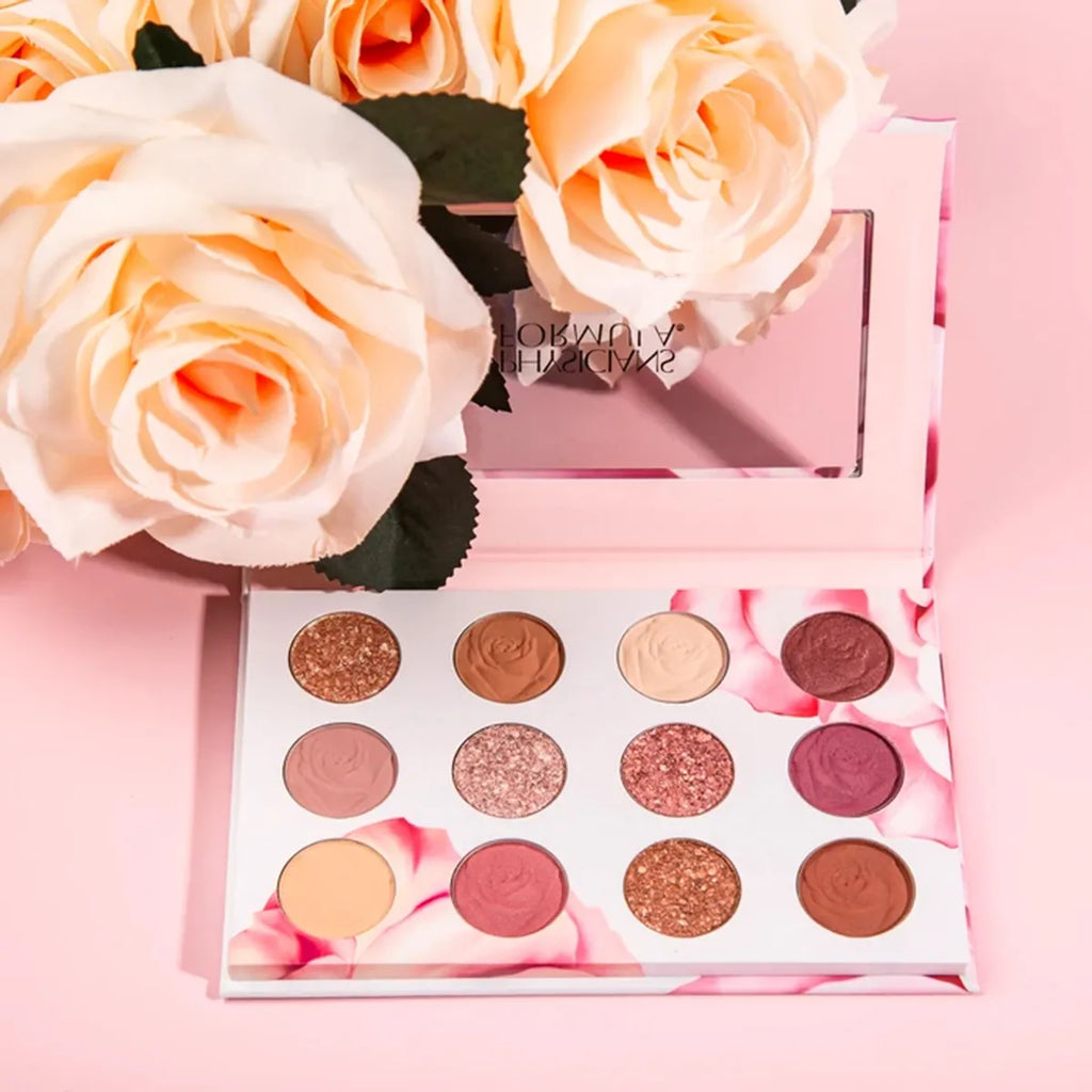 Physicians Formula eyeshadow palette with 12 rose-inspired shades and a floral design, displayed beside cream-colored roses