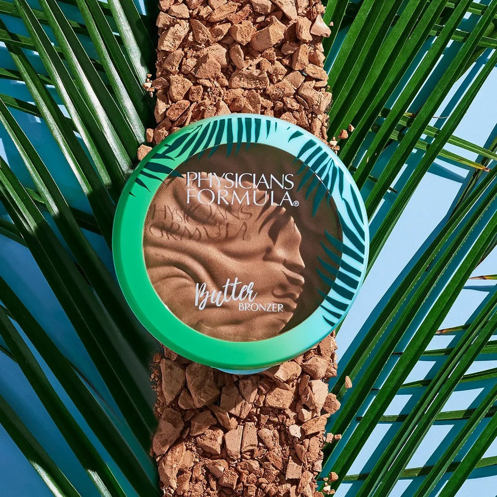 Physicians Formula Butter Bronzer in green tropical compact placed on crushed bronzer and palm leaves